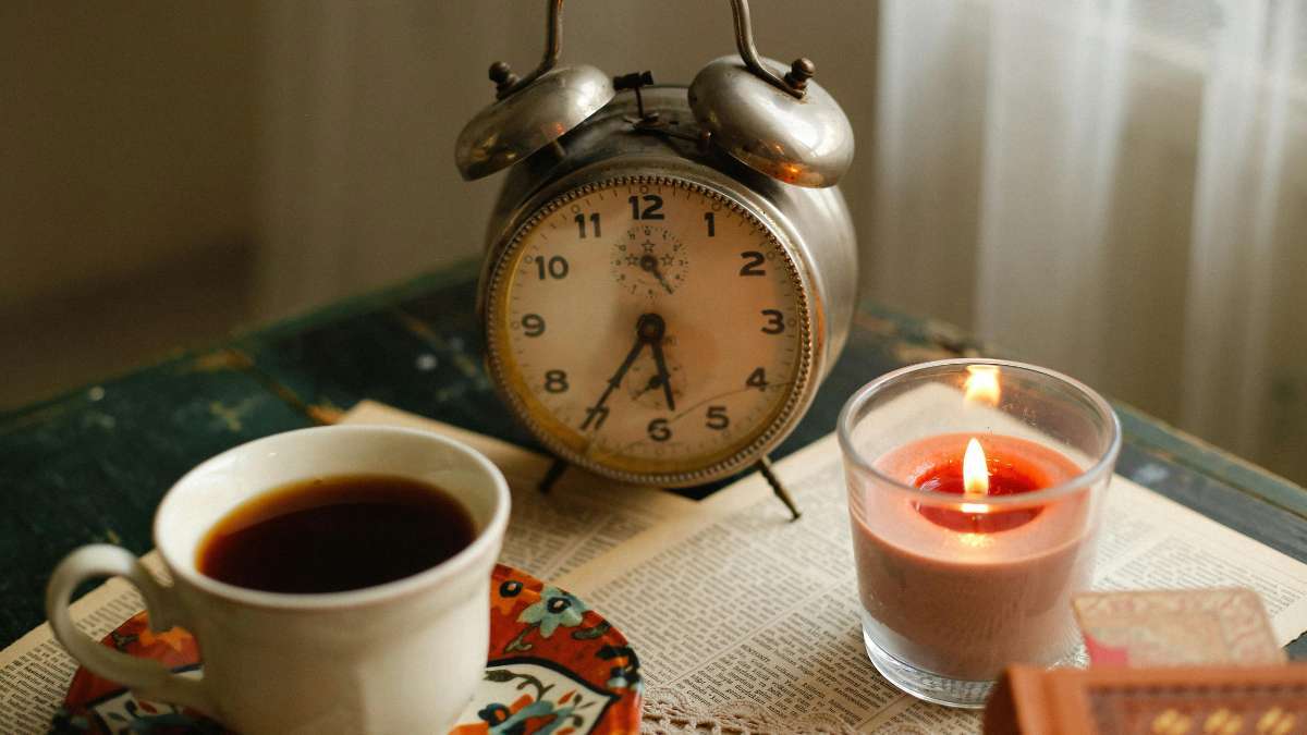 A soothing cup of tea and a lit candle next to a vintage alarm clock, representing a calm morning routine and nervous system regulation during the time change.